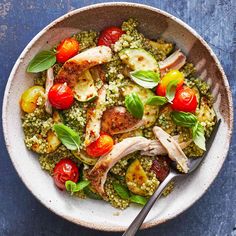 a white bowl filled with chicken, tomatoes and couscouse on top of a blue table