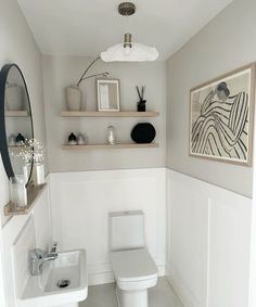 a white toilet sitting in a bathroom next to a sink under a framed art piece