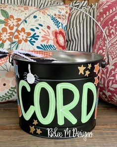 a black bucket with the word cord painted on it sitting in front of colorful pillows