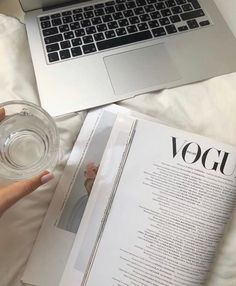 a person is reading a book and drinking water from a glass in front of their laptop