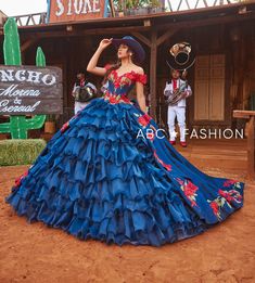 a woman in a blue and red dress is standing on the dirt near a sign