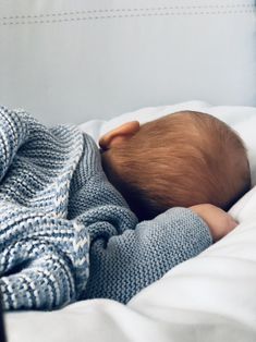 a baby wrapped in a blanket sleeping on top of a white bed with blue blankets