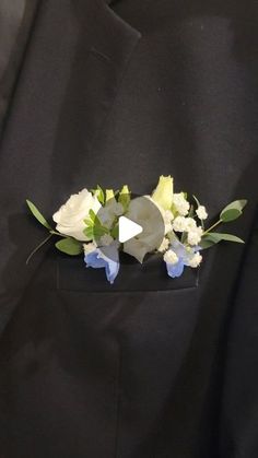 a boutonniere with white flowers and green leaves on the lapel of a black suit