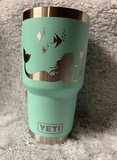 a yeti cup with an image of a mermaid and fish on the lid sitting on a fluffy surface