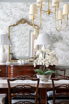 a dining room table with chairs and a vase on it's side next to a mirror