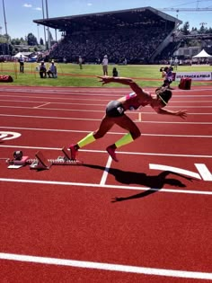 two female athletes in the middle of a race on a red track with people watching