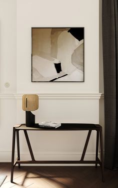 a black and white painting hanging on the wall above a wooden table with a lamp next to it