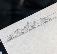 a piece of paper with a drawing of mountains and pine trees on the top of it