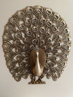 a metal peacock sculpture sitting on top of a white wall next to a wooden table