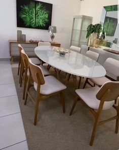 a dining room table with white chairs and a large painting on the wall behind it