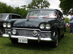 an old black car is parked in the grass