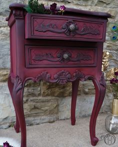 an ornately painted red nightstand with flowers on the top and bottom drawer, in front of a stone wall