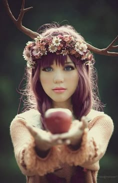 a girl with flowers on her head holding an apple