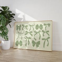 a green framed art piece sitting on top of a wooden floor next to a potted plant