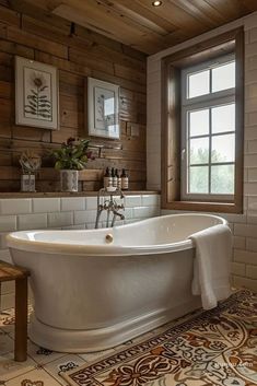 a white bath tub sitting under a window next to a wooden wall with pictures on it