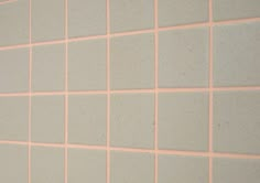 a bathroom with pink and white tiles on the wall next to a toilet paper dispenser