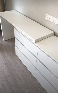 a white desk with drawers and two lights on the wall in an empty room next to a window