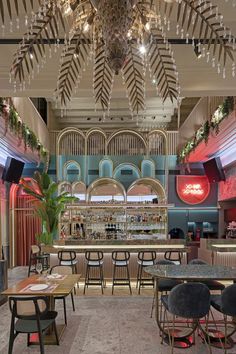 a bar with lots of stools and tables in front of the bar is lit by chandeliers that hang from the ceiling