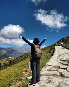 a woman standing on top of a grass covered hillside with her arms in the air