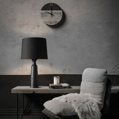 a table with a lamp and a chair in front of it, next to a clock on the wall