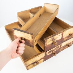 a hand holding a wooden drawer open to show it's drawers and the bottom section