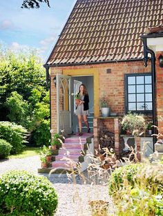 a woman standing in the doorway of a brick house with potted plants on either side