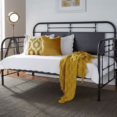 a metal daybed with yellow and white pillows on it's sides in a room