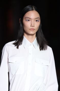 a model walking the runway with pastel blue eyelashes and is wearing a white dress shirt Fashion Week Fall 2023, Fall Beauty Trends, Fringe Styles, Curly Fringe, Prada Runway, 2024 Runway, Prada Fashion, Sleek Bun