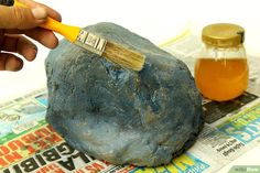 a person holding a paintbrush over a rock with honey in the jar on it