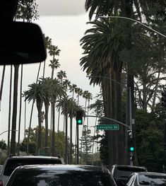 several cars are stopped at an intersection with palm trees in the background and green traffic lights