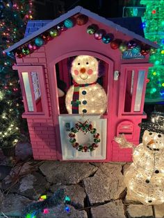 there is a small house with lights on it and a snowman in the doorway