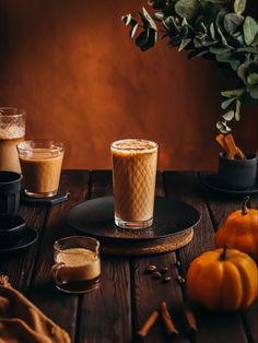 two glasses of coffee sitting on top of a table next to pumpkins and cinnamon sticks