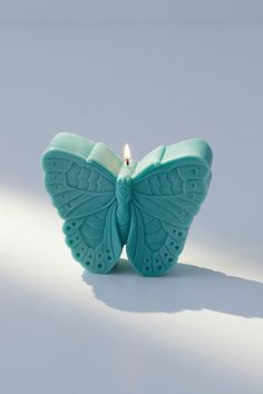 a teal colored butterfly shaped candle with a single lit candle in it's center