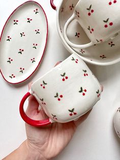 a hand holding a cup and saucer with cherries on it next to other dishes