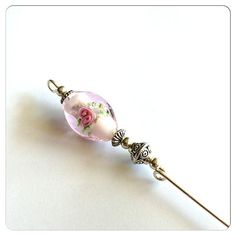 a pink flowered glass bead on a silver colored metal pin with an ornate design