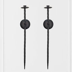 two black candles are standing next to each other on a white wall and one is in the shape of a candle holder