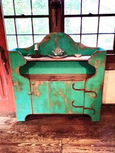 an old green painted dresser in front of a window with a cup and saucer on it