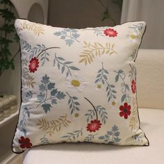 a white pillow with red, blue and yellow flowers on it sitting on a chair