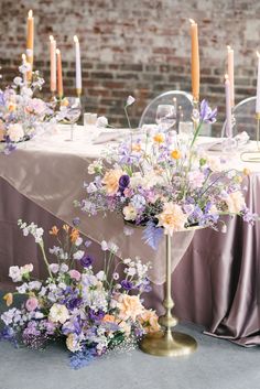 an arrangement of flowers and candles on a table in front of a brick wall at a wedding reception