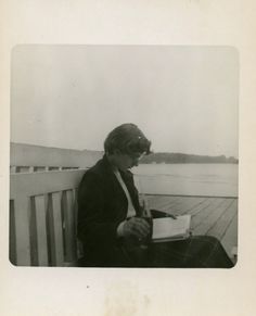 an old black and white photo of a woman sitting on a bench looking at a book