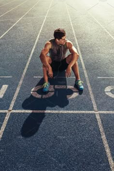 a man sitting on the edge of a running track listening to headphones