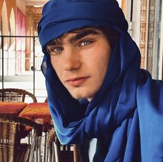 a young man wearing a blue scarf around his head and looking at the camera with an intense look on his face