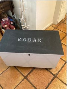 a black and white box with the word kodak written in chalk on it next to a small child