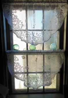 the window is decorated with lace and green glass balls on it's windowsill