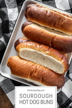 three hot dogs in buns on a white tray with the words sourdough hot dogs