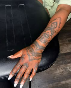 a woman's hand with tattoos on it sitting next to a black leather chair