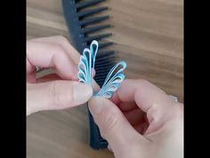 two hands are holding small blue scissors on a wooden table next to a black comb