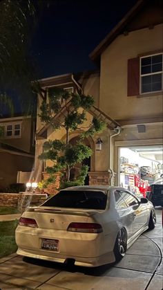 a white car is parked in front of a house at night with its lights on