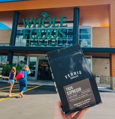 a person holding up a bag of coffee in front of a whole foods store with two women walking by