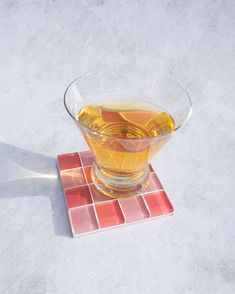 a glass filled with liquid sitting on top of a tiled counter next to a spoon